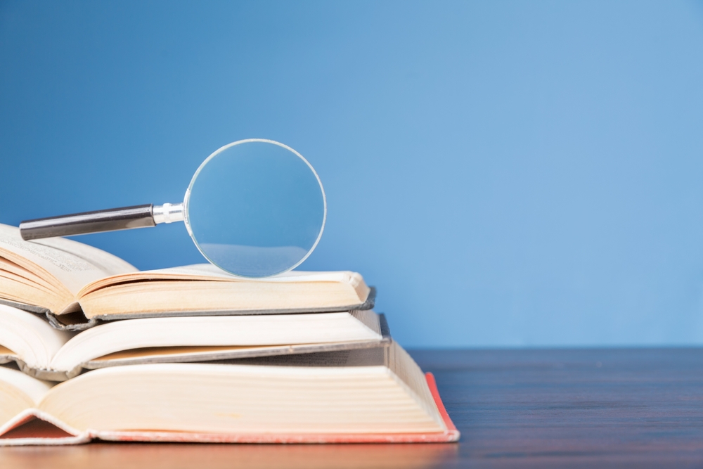 Stack-of-open-books-with-magnifying-glass-on-top