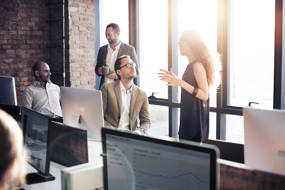 Coworkers-chatting-in-office-with-computers-lined-up-on-desks