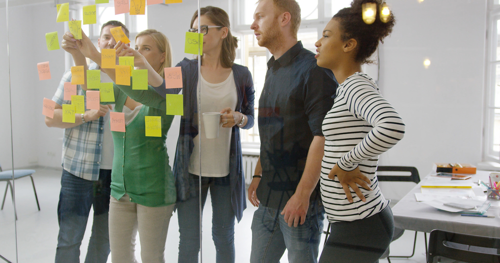 Team-of-people-organizing-sticky-notes-on-glass-wall.