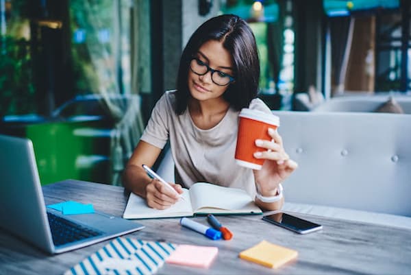 Young-woman-drinking-coffee-and-writing-in-a-notebook