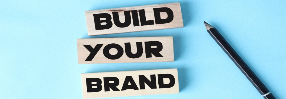 Wooden blocks spelling Build Your Brand next to a pencil on a blue background